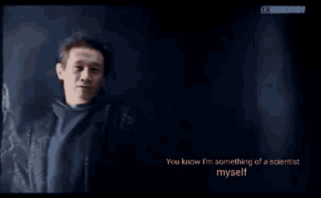 a man in a black jacket is standing in front of a dark background and says you know i 'm something of a scientist