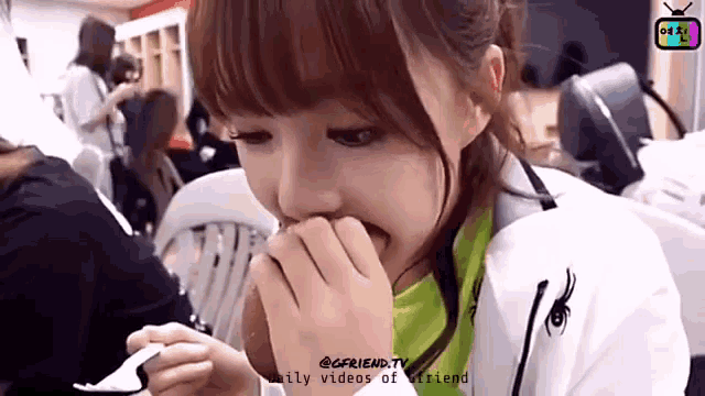 a girl is eating a spoonful of food with a tv in the background