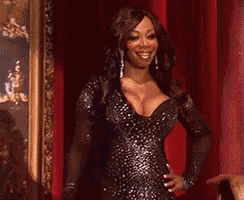a woman in a black dress is standing in front of a red curtain .