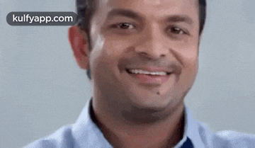 a close up of a man 's face smiling while wearing a blue shirt and tie .
