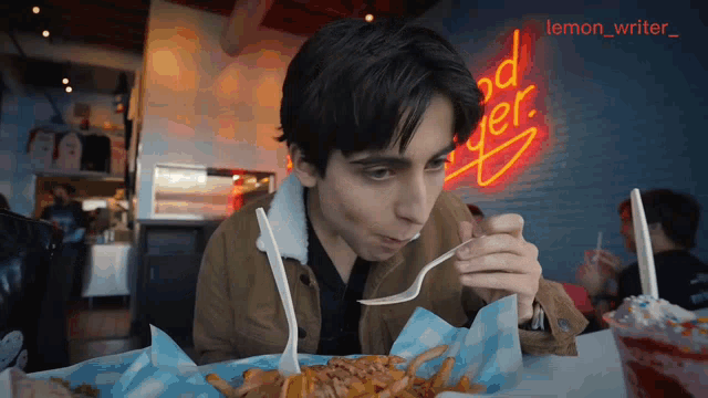 a man eating french fries with a fork in front of a neon sign that says good burger