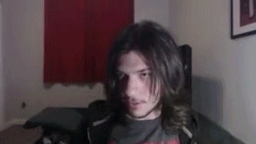 a young man with long hair and a mustache is sitting in a chair .