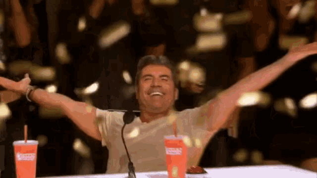 a man with his arms outstretched is sitting at a table with two coca cola drinks