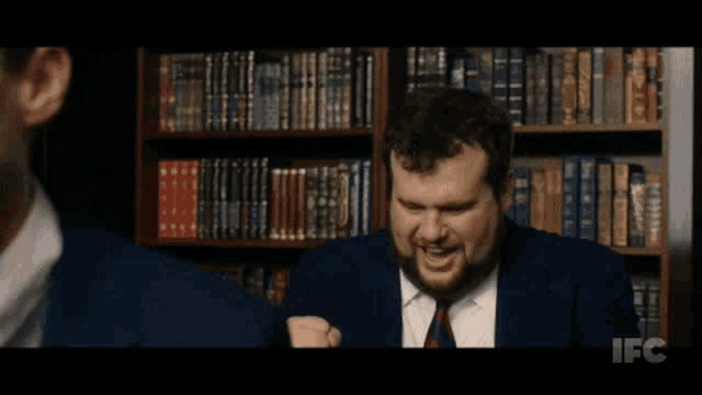 a man in a suit and tie is laughing in front of a bookshelf with ifc written on it