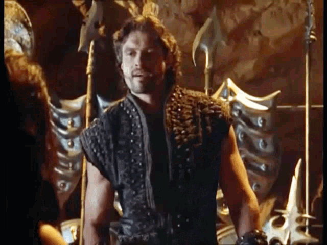 a man in a leather vest is standing next to a woman in a cave with a sword .