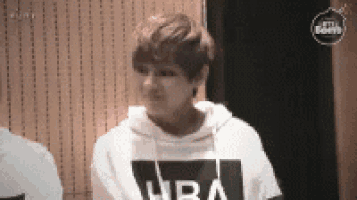 a young man wearing a white hoodie with the word nba on it is sitting in front of a wooden wall .