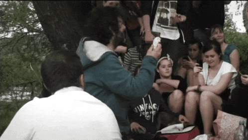 a group of people are gathered under a tree and one of them is wearing a vintage tokyo shirt