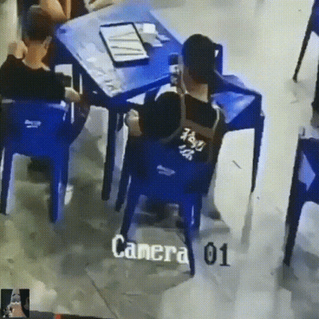 a person sitting at a table in front of a camera that says camera 01