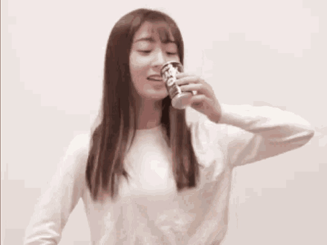 a woman in a white sweater is standing in front of a white wall with her arms outstretched .