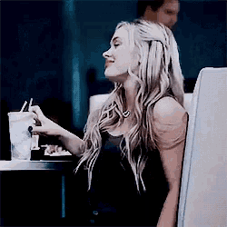 a woman is sitting at a table with a drink in her hand and a straw .