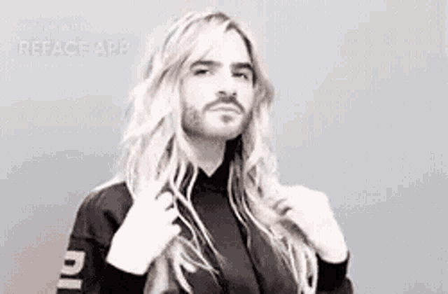 a man with long blonde hair and a beard is wearing a black jacket and a black shirt .
