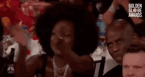 a woman with an afro is sitting at a table with other people at a golden globe awards event .