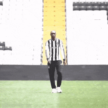 a man wearing a black and white striped shirt is standing on a soccer field .