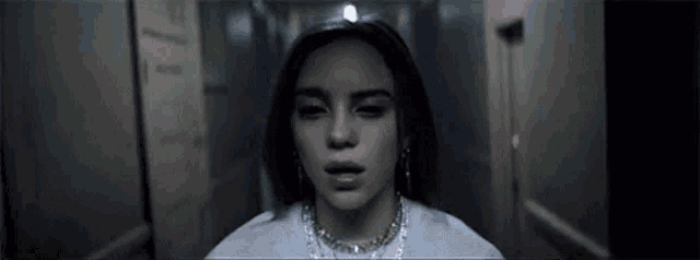 billie eilish is standing in a hallway with her eyes closed and looking at the camera .