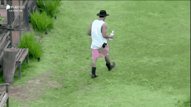 a man in a cowboy hat and pink shorts is walking through a grassy field ..