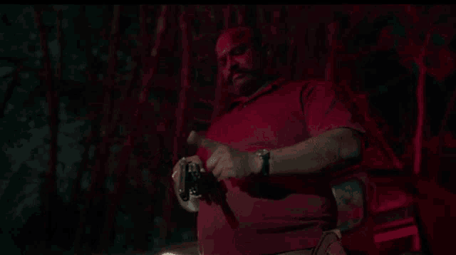 a man in a red shirt is holding a gun in his hand in the dark .