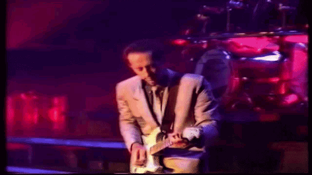 a man in a suit playing a guitar on stage