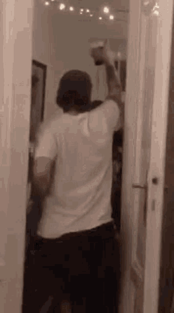 a man in a white shirt is standing in a doorway holding a glass .