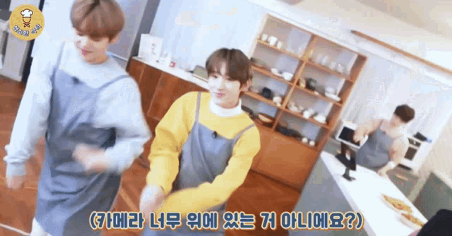 a group of people in aprons are dancing in a kitchen and one of them is wearing a yellow sweater