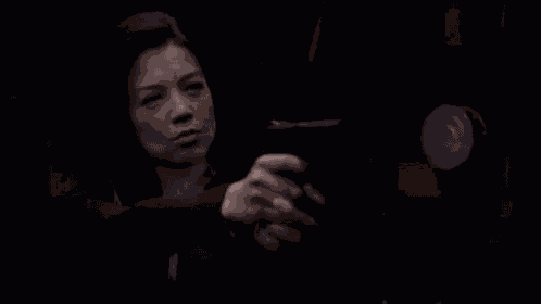 a woman is holding a gun in a dark room and looking at it .