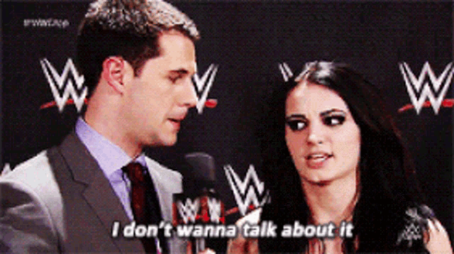 a man in a suit and tie is talking to a woman in front of a wrestling logo