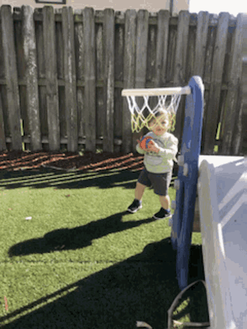 a little boy is playing basketball in a backyard