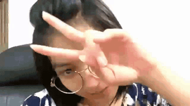 a young woman wearing glasses is making a peace sign with her hands .