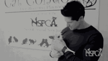 a man is holding a kitten in front of a sign that says nspca
