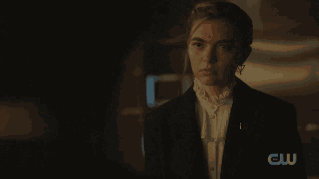 a woman stands in a dark room with a cw logo on her shoulder