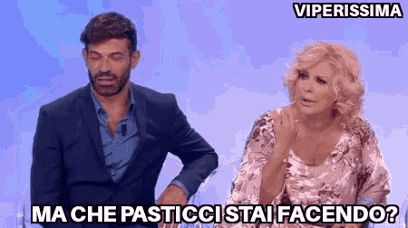 a man in a suit and a woman in a dress are sitting next to each other on a television show .