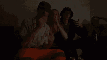a group of people are sitting on a couch in a dark room smoking cigarettes .