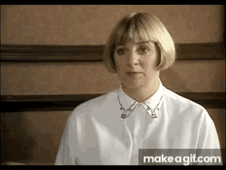 a woman wearing a white shirt with a gold collar looks at the camera with a make a gif.com button below her