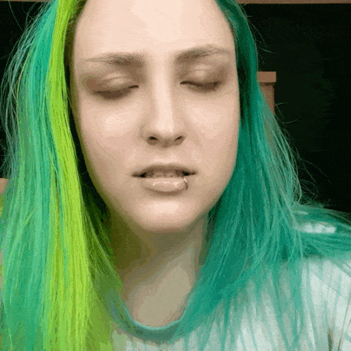 a woman with green hair has her eyes closed and a piercing in her lip