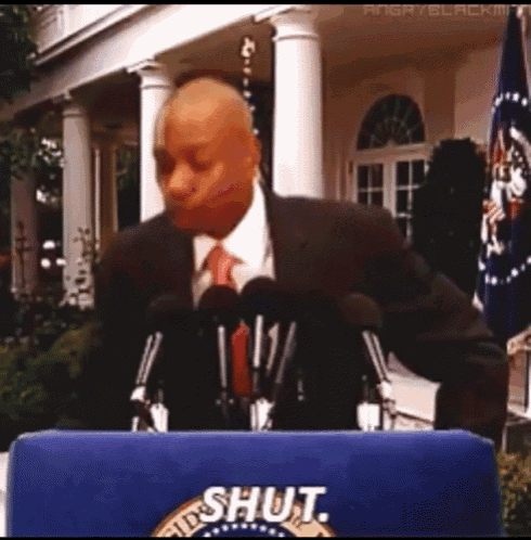 a man in a suit and tie stands at a podium with the word shut on it
