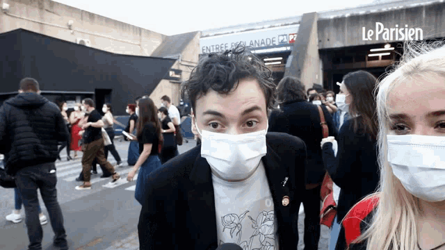 a man wearing a face mask stands in front of a building that says le parisien on it
