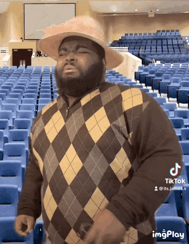 a man wearing a plaid sweater and a hat stands in front of empty auditorium seats
