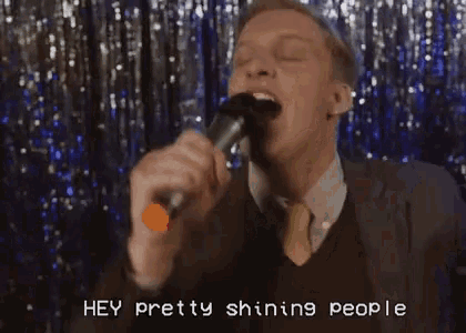 a man in a suit singing into a microphone with the words hey pretty shining people below him