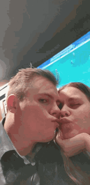 a man and a woman are kissing in front of a tv screen