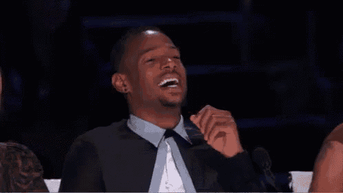 a man in a suit and tie is laughing with his hand on his chin .