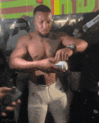 a shirtless man is standing in front of a crowd holding a bottle .