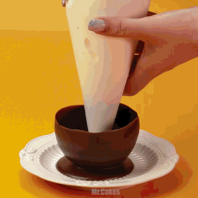 a person is pouring frosting into a chocolate cup on a plate which says mr.cakes on the bottom