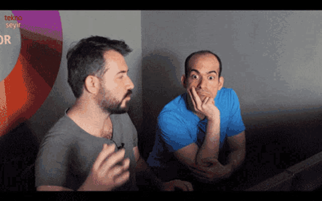 two men sitting in front of a sign that says tekno seyir