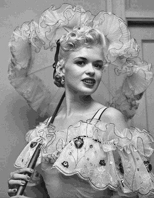 a woman in a ruffled dress holds an umbrella in a black and white photo