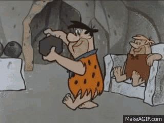 a cartoon of flintstone holding a large rock while another caveman sits on a couch .