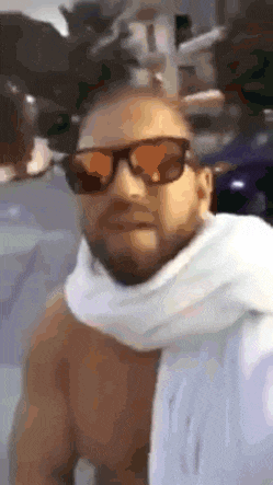 a shirtless man wearing sunglasses and a white scarf around his neck .