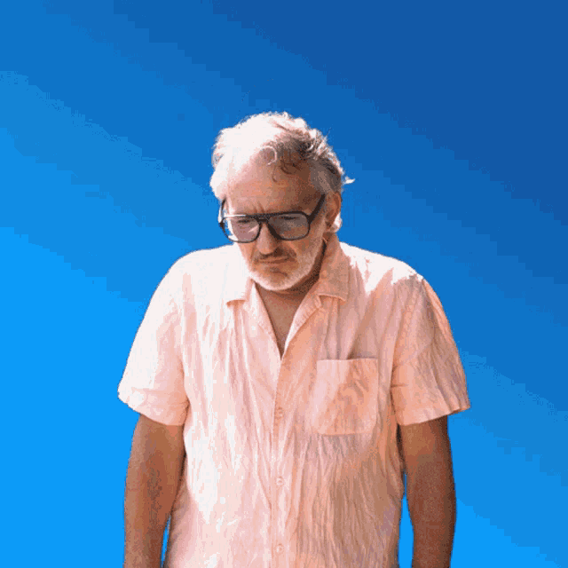 a man wearing glasses and a pink shirt looks down