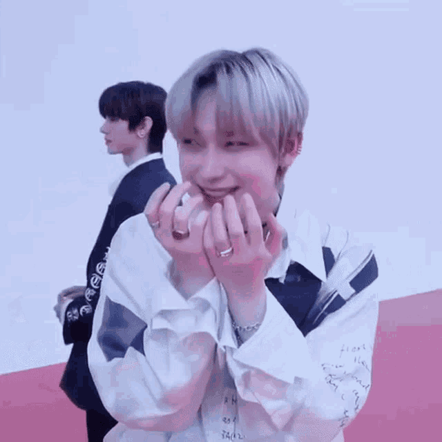 a man in a white shirt is making a heart with his hands while another man stands behind him .