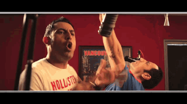 a man wearing a hollister shirt is singing into a microphone in front of a picture of vancouver