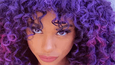 a close up of a woman with purple curly hair .