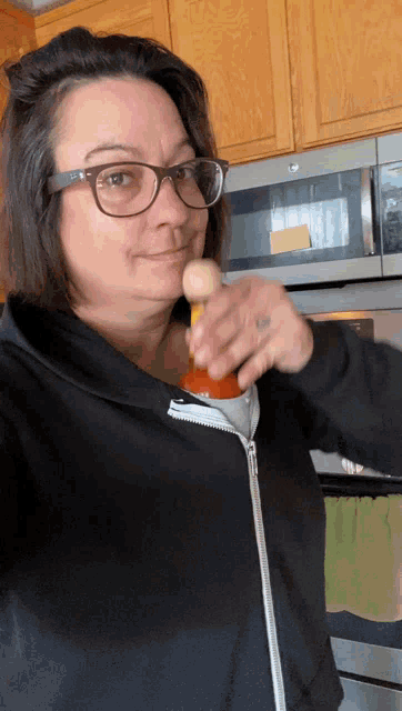 a woman wearing glasses is opening a bottle of hot sauce in a kitchen